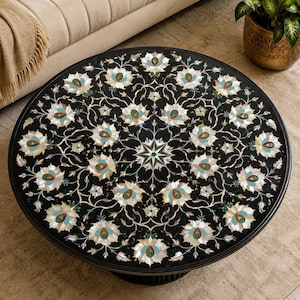 Könnte beinhalten: Ein runder schwarzer Tisch mit einem komplexen Einlegemuster aus weißen, türkisfarbenen und orangefarbenen Blumenmotiven, die symmetrisch um einen zentralen Stern angeordnet sind, verbunden durch feine weiße Rankendetails.