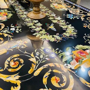 Pode incluir: Um tampo de mesa de mármore preto com intrincados desenhos florais incrustados com pedras coloridas. O design apresenta flores, folhas e videiras em tons de amarelo, verde, azul e vermelho.