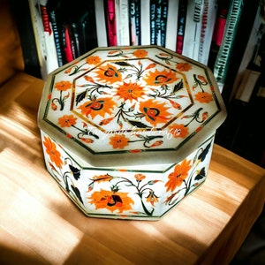 May include: Octagonal white marble box with intricate floral designs in orange, green, and gold. The box is decorated with a floral pattern and the text "Tangerine handicrafts".