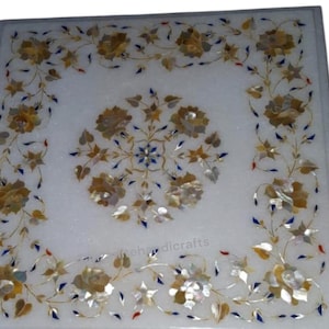 May include: White marble square table top with intricate floral inlay design. The design features gold, white, and blue accents. The table top is approximately 16 inches by 16 inches.
