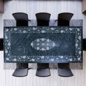 May include: A dark green marble dining table with a floral design inlaid with mother of pearl. The table is surrounded by six black chairs.