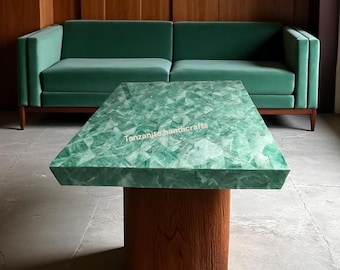 Puede incluir: Una mesa de centro rectangular con una superficie verde facetada y una base de madera. La mesa está frente a un sofá de terciopelo verde. El texto "tanzanite handicrafts" es visible en la mesa.