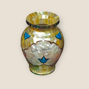 May include: A decorative vase with a mosaic design. The vase features a yellow and white mother-of-pearl pattern, with blue accents and a floral design. The text "Tanzanite handicrafts" is visible on the vase.