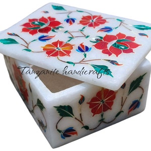 May include: White marble box with a hinged lid. The box is decorated with intricate floral designs in red, green, blue, and gold. The text "Tanzanite handicrafts" is visible on the box.