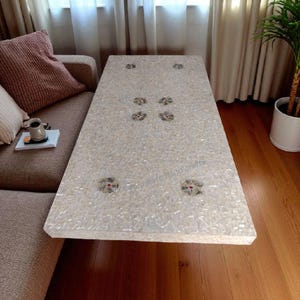 Pode incluir: Mesa de centro retangular branca com um design de mosaico de conchas. A mesa apresenta detalhes florais decorativos e está colocada numa sala de estar. A mesa tem aproximadamente 122 cm de comprimento e 61 cm de largura.