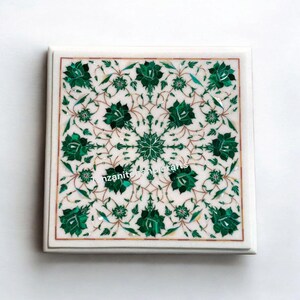 May include: Square white marble coaster with a detailed floral inlay design. The design features green flowers and leaves with brown accents, creating a symmetrical pattern. The coaster has a polished finish and a decorative border.