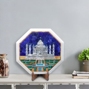 Könnte beinhalten: Oktogonale weiße Marmorplatte mit einer Mosaik-Einlage, die das Taj Mahal darstellt. Das Mosaik hat blaue, grüne und goldene Akzente. Die Platte steht auf einem Holzständer.