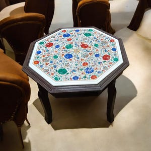 Könnte beinhalten: Achteckiger Tisch mit einer weißen Marmorplatte mit einem farbenfrohen Blumendesign. Der Tisch hat ein dunkles Holzgestell mit vier Beinen.