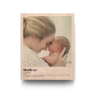 May include: A wood print with a photo of a mother and her newborn baby. The photo shows the mother holding the baby close and they are both looking at each other. The print has the word "Mother" and its definition printed below the photo.