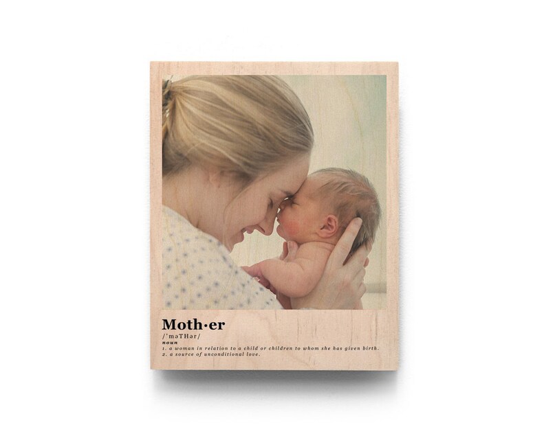 May include: A wood print with a photo of a mother and her newborn baby. The photo shows the mother holding the baby close and they are both looking at each other. The print has the word "Mother" and its definition printed below the photo.