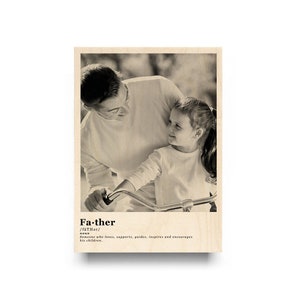 May include: A black and white photo of a father and daughter. The father is looking down at his daughter, who is sitting on a bicycle. The photo is printed on a wooden background with the word "Father" and its definition.