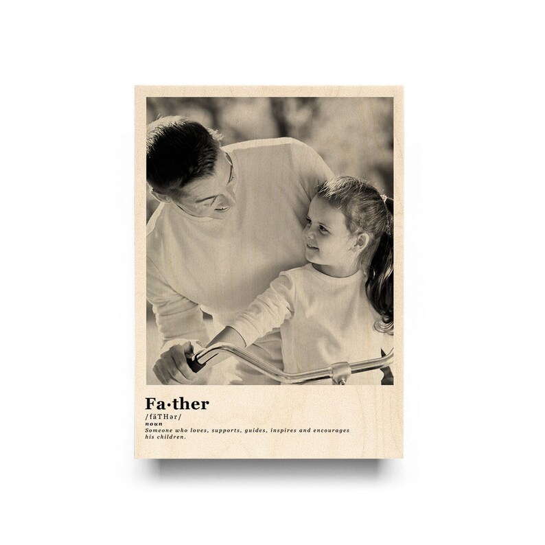 May include: A black and white photo of a father and daughter. The father is looking down at his daughter, who is sitting on a bicycle. The photo is printed on a wooden background with the word "Father" and its definition.