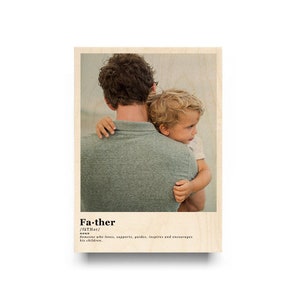 May include: A father and son are hugging. The father is wearing a green shirt and the son is wearing a white shirt. The image is in a wood frame with the word "Father" and its definition.
