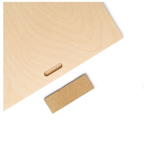 May include: A light brown wooden board with a rectangular cutout in the center. A smaller, rectangular piece of brown wood is placed on a white surface.