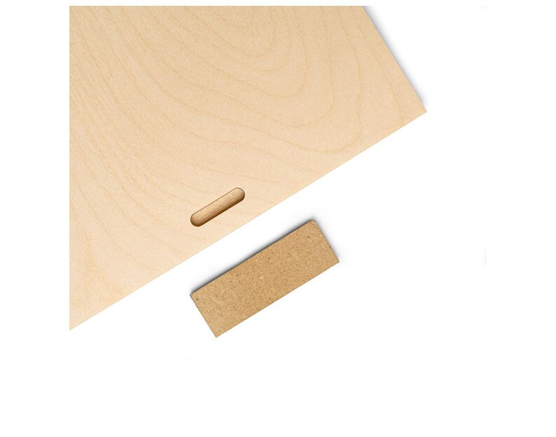 May include: A light brown wooden board with a rectangular cutout in the center. A smaller, rectangular piece of brown wood is placed on a white surface.