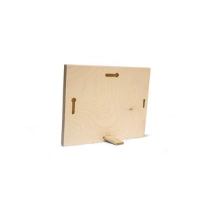 May include: A light wood photo frame with a stand on the back. The frame has two holes on the back for hanging.