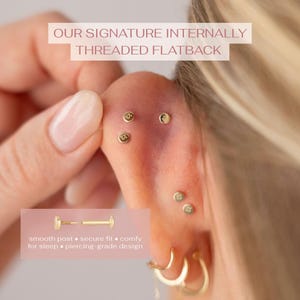 May include: Gold flatback stud earrings with internally threaded posts. The jewelry features small circular discs with a subtle engraved detail. Text on the image reads: OUR SIGNATURE INTERNALLY THREADED FLATBACK, smooth post, secure fit, comfy for sleep, piercing-grade design.