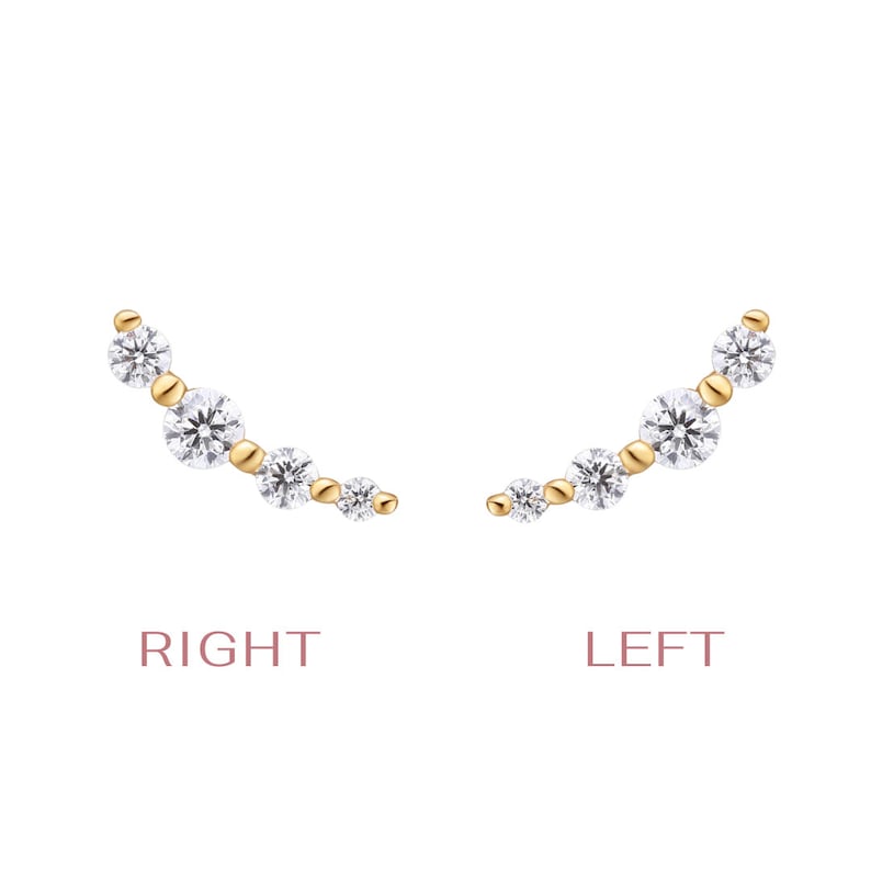 May include: A pair of gold ear climbers featuring four round-cut clear stones of varying sizes arranged in a curved line. The left and right earrings are labeled with the text RIGHT and LEFT in a light pink font below each respective piece.