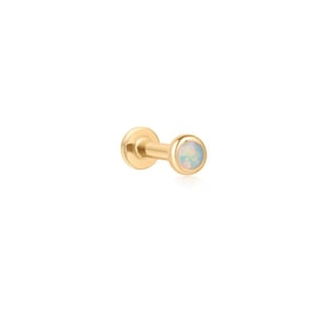 May include: A gold-toned flat back stud earring featuring a circular bezel setting. The front of the stud is inlaid with a round, iridescent opal stone that displays subtle flashes of blue, pink, and white color against the polished metal finish.