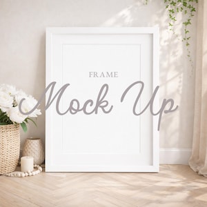 May include: A white picture frame with the text "FRAME" and "Mock Up" in a light gray script. The frame is propped up against a wall, with a woven basket of white flowers, a vase, and a candle to the left.
