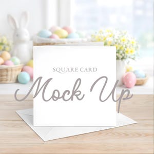 Op de afbeelding: Een witte vierkante kaartmockup met de tekst "SQUARE CARD" en "Mock Up" in een scriptlettertype. De kaart ligt op een witte envelop op een houten oppervlak. Paaseieren en een konijnenbeeldje staan op de achtergrond.