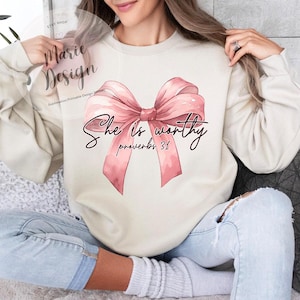 May include: A white sweatshirt with a pink bow and the text "She is worthy Proverbs 31" printed on it.