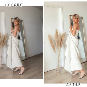 May include: A woman in a white linen dress stands in a room with a mirror and a vase of dried pampas grass. She is wearing white heels and has her hair pulled back.