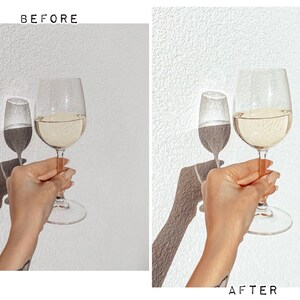 May include: A hand holding two wine glasses, one larger than the other, both filled with white wine. The glasses are on a white background.