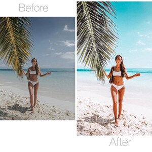 May include: A woman in a white bikini stands on a sandy beach with a turquoise ocean and blue sky in the background. Palm fronds frame the scene. The woman is holding a brown and white bag.
