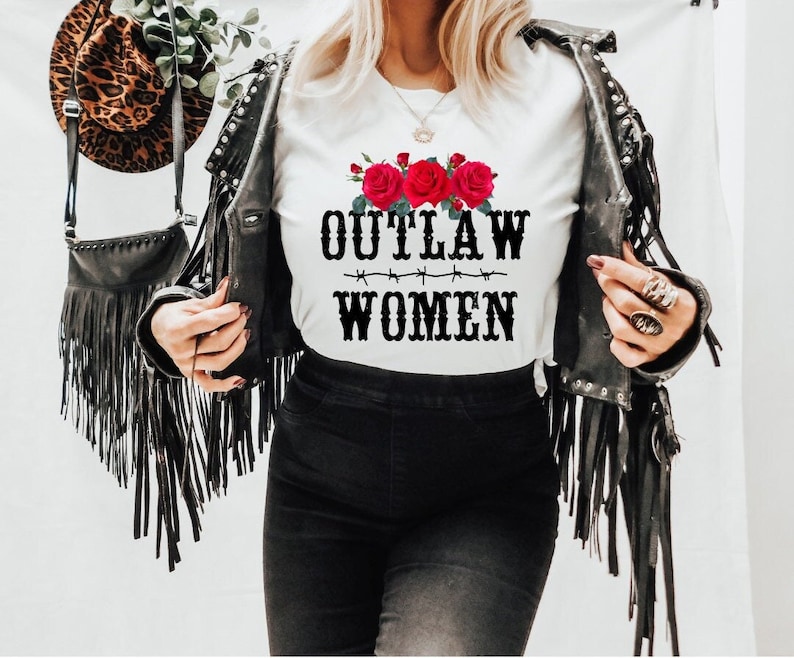 Pode incluir: Camiseta branca com um gr&aacute;fico preto que diz "OUTLAW WOMEN" com um design de arame farpado e rosas vermelhas.