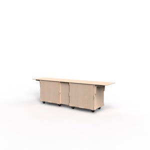 May include: A light-colored, rectangular table on wheels. The table has a long, flat surface and a series of connected, box-like structures underneath. The table is made of a light-colored material, possibly wood, and is designed for storage or display.