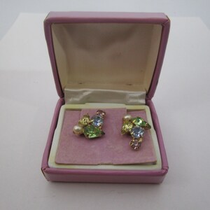 May include: A pair of vintage earrings in a pink box. The earrings are made of gold tone metal and feature a cluster of pastel-colored rhinestones and a single pearl.