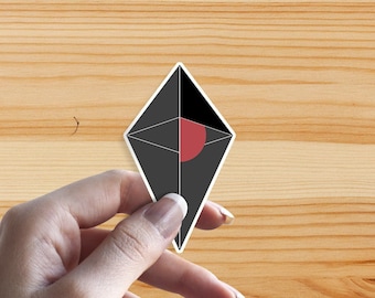 Può includere: Un adesivo nero e bianco con un cerchio rosso al centro, a forma di diamante. L'adesivo è tenuto da una mano.