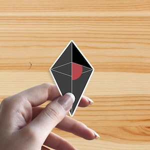 Peut inclure: Un autocollant noir et blanc avec un cercle rouge au centre, en forme de diamant. L'autocollant est tenu par une main.