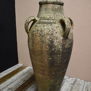 May include: A large, weathered terracotta pot with two handles on each side. The pot is a light brown colour with dark brown and grey streaks and spots.