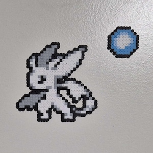 May include: A pixel art design featuring a white creature with gray accents and black outlines, along with a blue orb. The artwork is created using small, colorful beads, giving it a textured appearance. The design is likely inspired by video games.