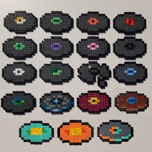 May include: A collection of 16 colourful, round, and oval-shaped bead sprites. The sprites are made of small, colourful beads and feature various designs, including flowers, eyes, and geometric patterns.