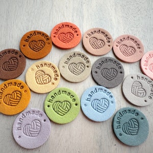 Pode incluir: Conjunto de 14 etiquetas redondas de couro feitas à mão com o texto "handmade" e um design de coração estilizado. As etiquetas são de várias cores, incluindo marrom, laranja, bege, azul claro, verde e cinza.