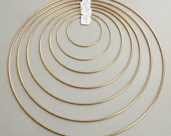Puede incluir: Un conjunto de seis aros metálicos de color dorado dispuestos de forma concéntrica. Cada aro presenta una estructura de alambre circular, fina y lisa. Una pequeña etiqueta de papel blanco con texto impreso está sujeta en la parte superior.