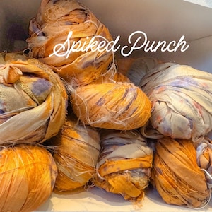May include: A collection of rolled fabric bundles in shades of orange, yellow, and cream. The fabric appears to be silk or a similar material, with a slightly textured surface. The text "Spiked Punch" is written in a cursive font across the image.