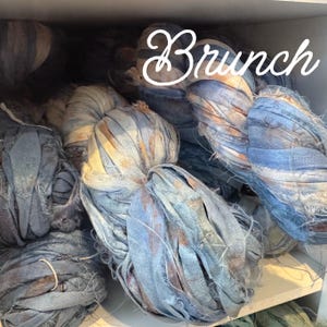 May include: A collection of blue and tan fabric ribbons, tightly wound and displayed on a shelf. The word "Brunch" is written in a cursive font across the top of the image. The ribbons have a distressed, textured appearance.