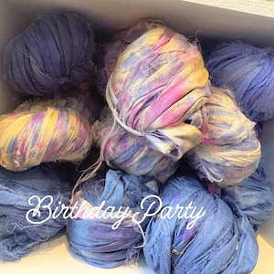 May include: A collection of blue and multi-colored fabric ribbon spools. Some spools are solid blue, while others have pink, yellow, and purple tie-dye patterns. The text "Birthday Party" is written in white script across the bottom.