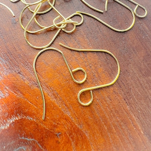 May include: A close-up of a pile of gold-colored earring hooks. The hooks are made of metal and have a simple, elegant design.