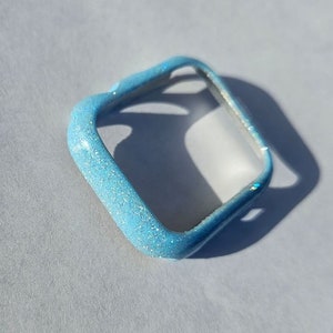 May include: A light blue glitter watch case for an Apple Watch.
