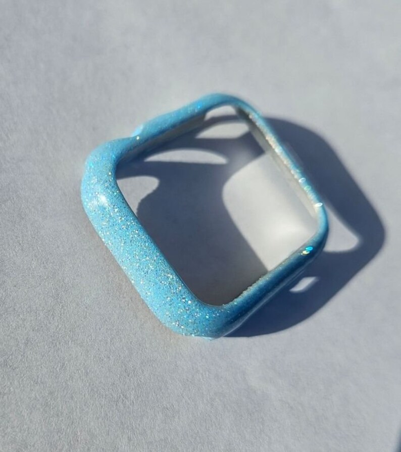 May include: A light blue glitter watch case for an Apple Watch.
