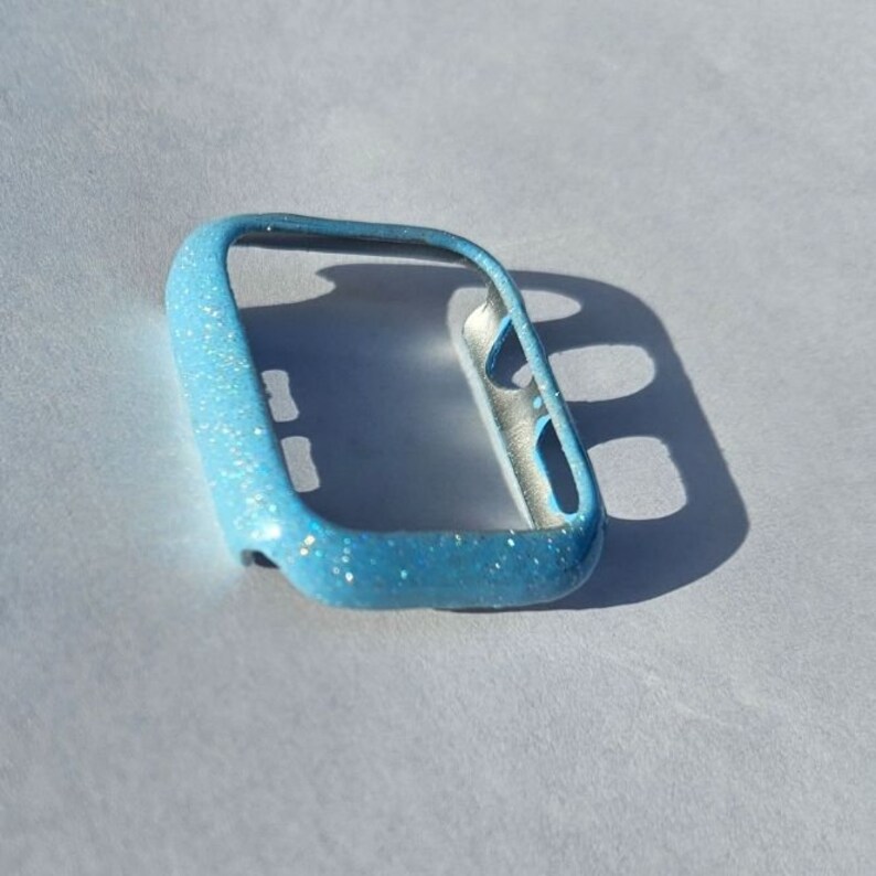 May include: A light blue glitter Apple Watch case. The case is made of a hard plastic material and has a clear back.