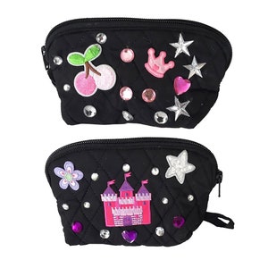 May include: Two black quilted makeup bags with zipper closures. The top bag has pink and white cherry, crown, star, and heart embellishments. The bottom bag has a pink castle, flower, star, and heart embellishments.