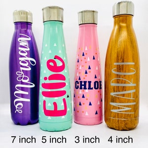 K&ouml;nnte beinhalten: Vier Edelstahl-Wasserflaschen mit verschiedenen Farben und Designs. Die Flaschen sind mit den Namen "Ellie", "Chloe", "Marci" und "Andie" beschriftet. Die Flaschen sind 17,8 cm, 12,7 cm, 7,6 cm und 10,2 cm hoch.