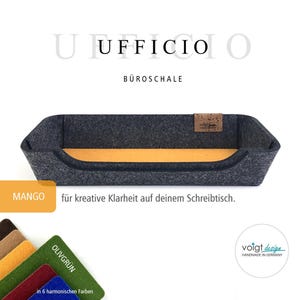 Könnte beinhalten: Ein grauer Filz-Schreibtisch-Organizer mit einem gelben Filz-Boden. Der Organizer ist mit "UFFICIO BÜROSCHALE MANGO" und "für kreative Klarheit auf deinem Schreibtisch." beschriftet.