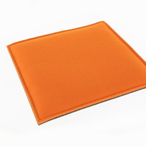 Op de afbeelding: Oranje gevoerd kussen met een grijze rand. Het kussen is rechthoekig en heeft een zachte, pluche textuur.